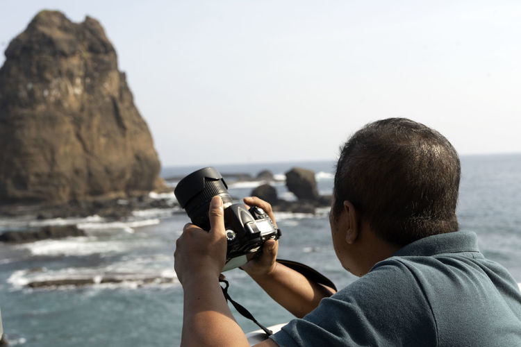 Rear view of man photographing on rock at beach