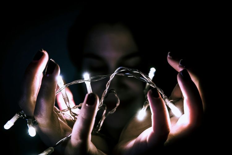 Close-up of woman holding illuminated string lights in darkroom