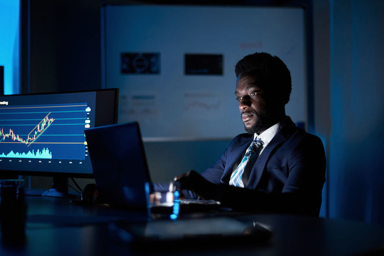 Black employee working on laptop in dark office