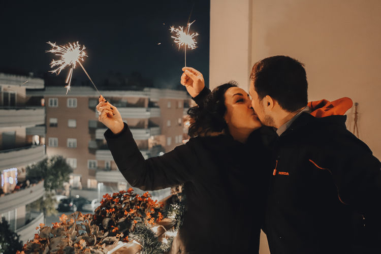 Couple holding illuminated sparklers while kissing