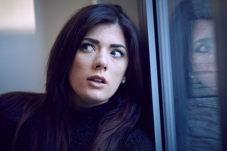 Close-up of worried woman looking away by window