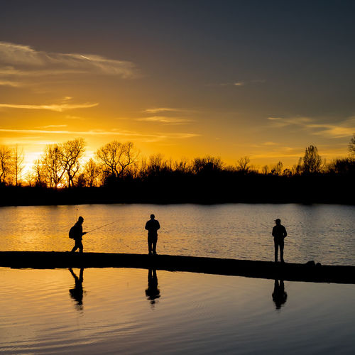 Silhouette people fishing at lake against sky during sunset