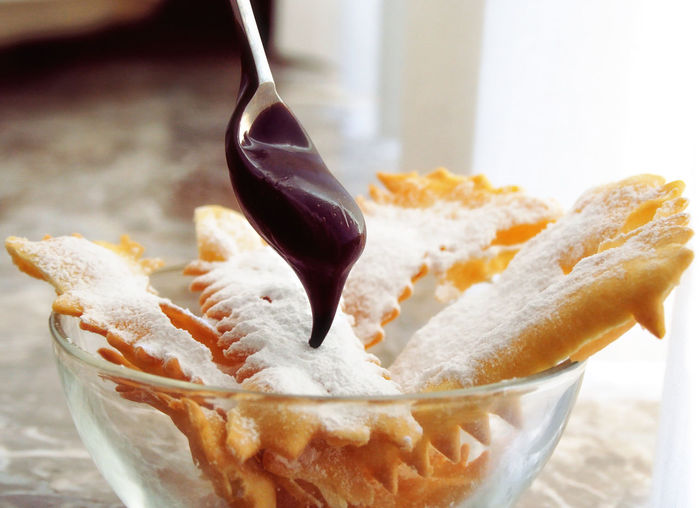 Frappe - typical italian carnival fritters dusted with powdered sugar , with a spoon full chocolate.