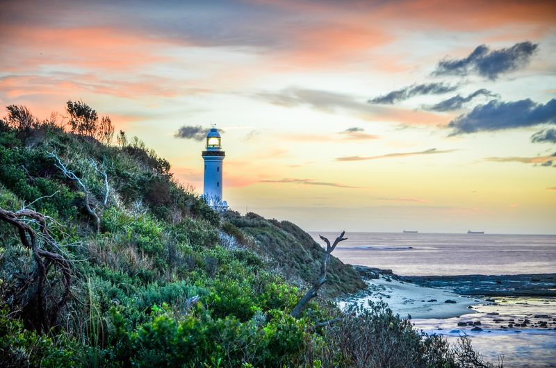 Lighthouse on rock against sky during sunset