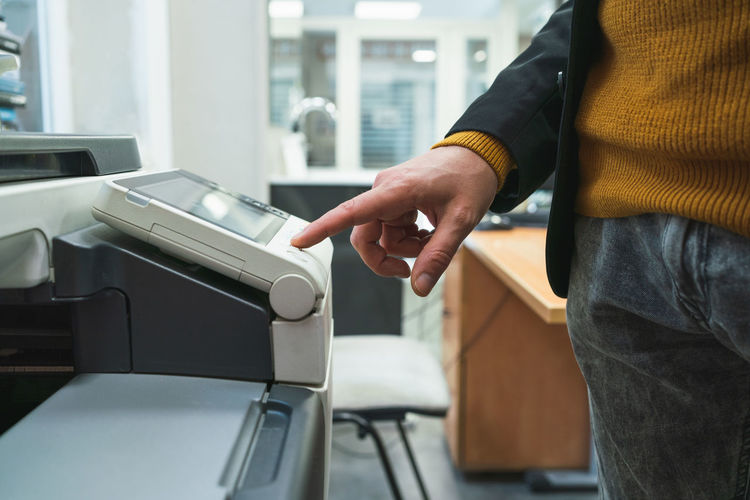 Close-up shot of a male hand clicking the button on a modern printer in a store