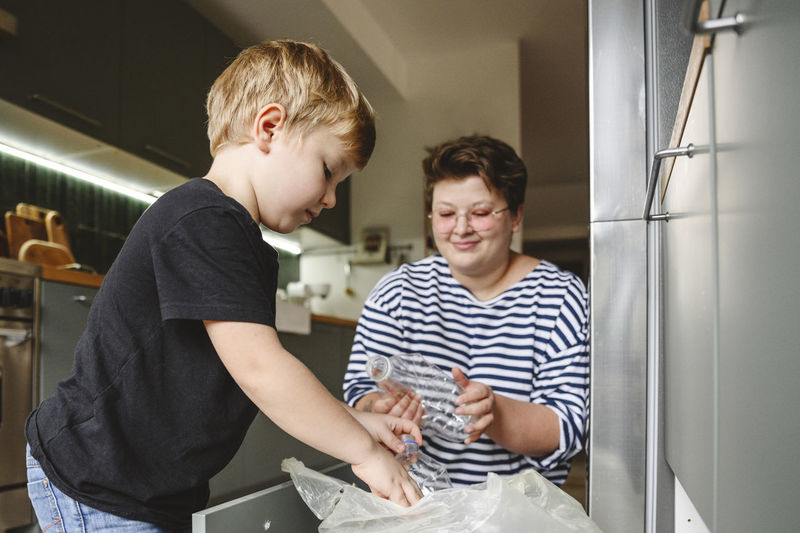 Mother and son sorting plastic garbage in kitchen at home