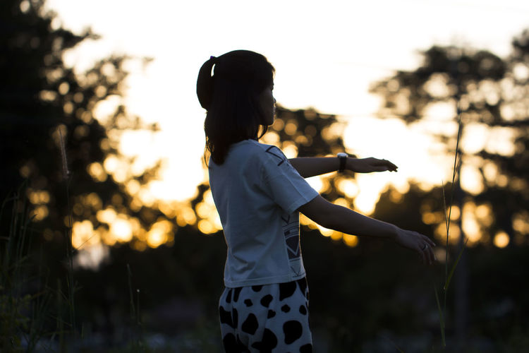 Young woman exercising against silhouette trees during sunrise
