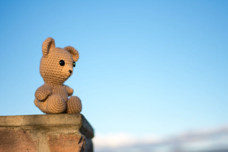 Low angle view of teddy bear on retaining wall against clear blue sky