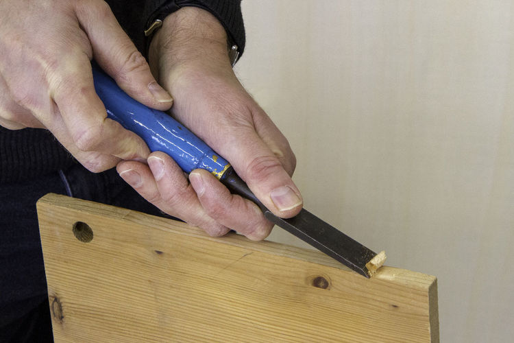 Cropped hands of man chiseling wood at workshop