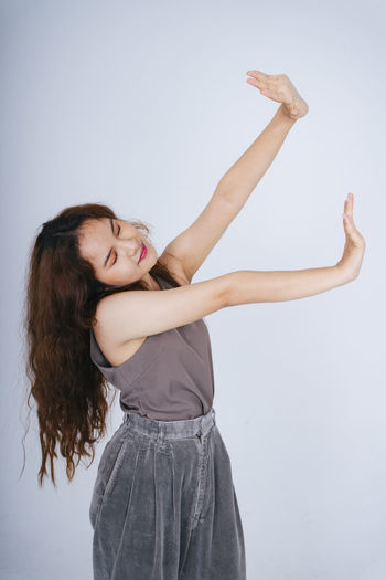 Smiling young woman with arms raised against gray background