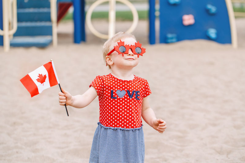 Cute girl wearing sunglasses while holding flag on sand