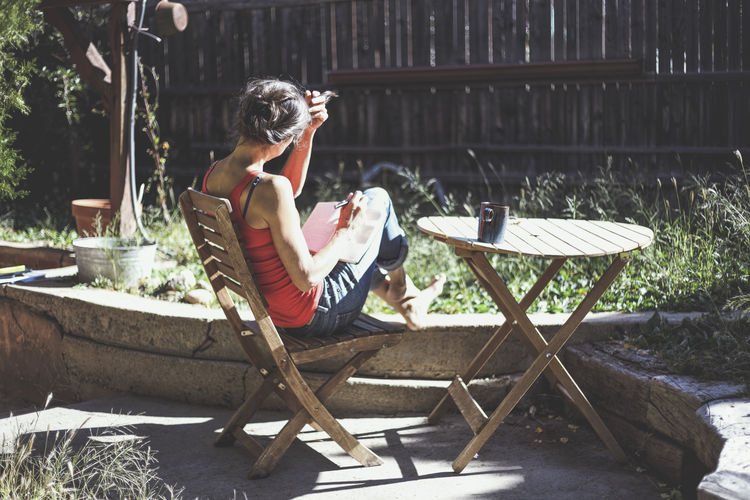 Woman with book sitting on chair at yard