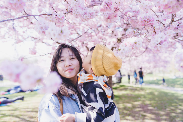A mom held her boy under pink cherry blossom. 