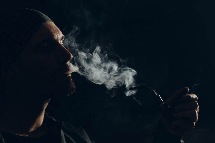 Portrait of young man smoking cigarette against black background