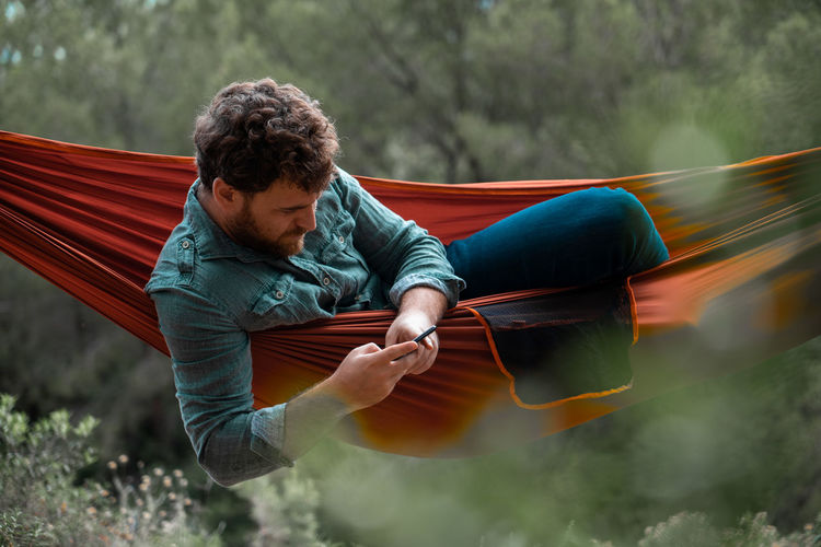 Man sitting using smart phone while on hammock in forest
