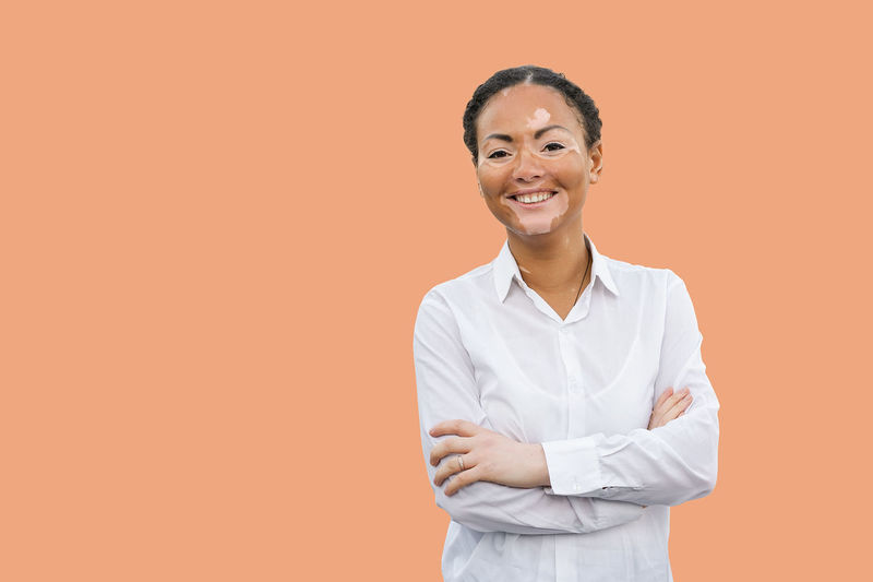 Portrait of young woman suffering from dermatitis standing against orange background
