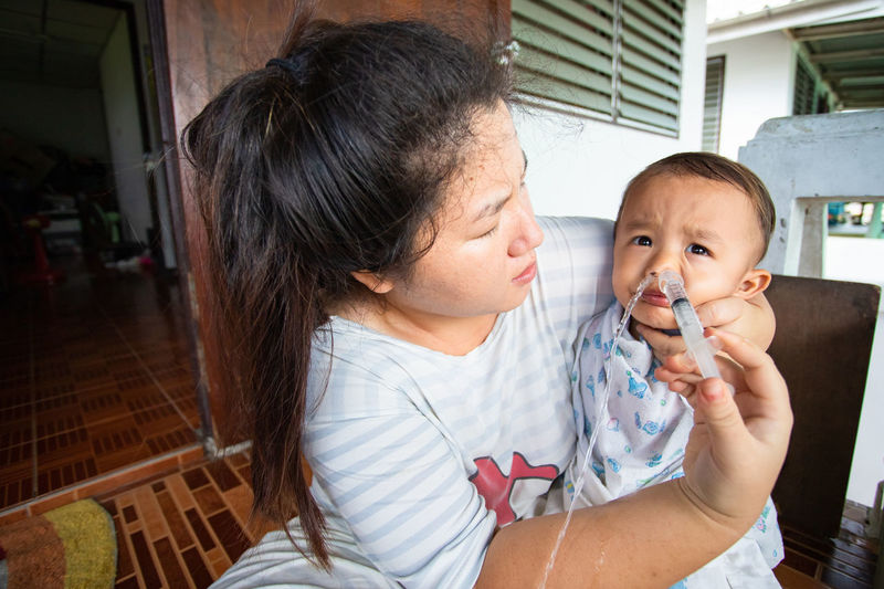 Mother inserting medicine to son through nose at home