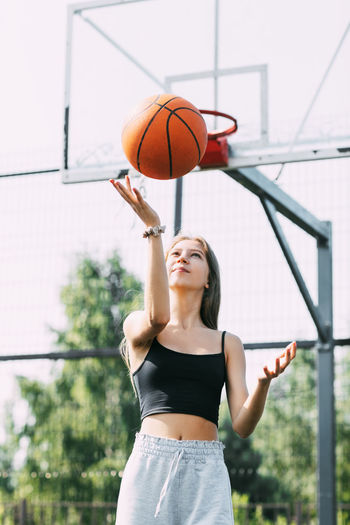 A beautiful teenage girl throws a basketball up during a workout on a sports field 
