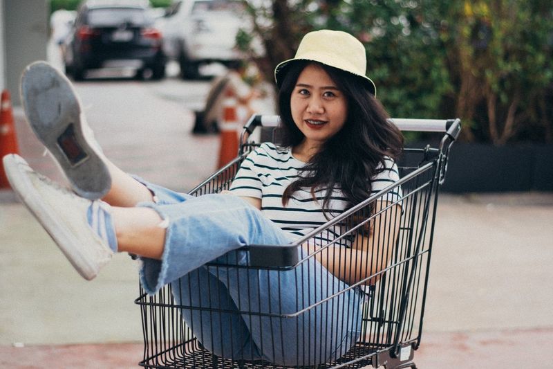 Portrait of smiling young woman sitting in shopping cart