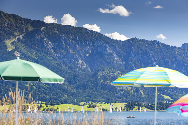 Parasols by forggensee lake against tegelberg mountain