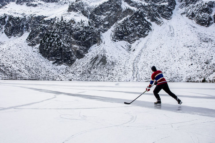 Unrecognizable hockey player ice skating on frozen lake near mountain