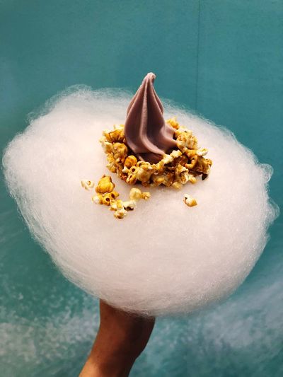 Cropped image of hand holding cotton candy with popcorn and whipped cream