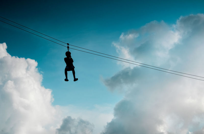 Low angle view of man hanging on zip line against sky 