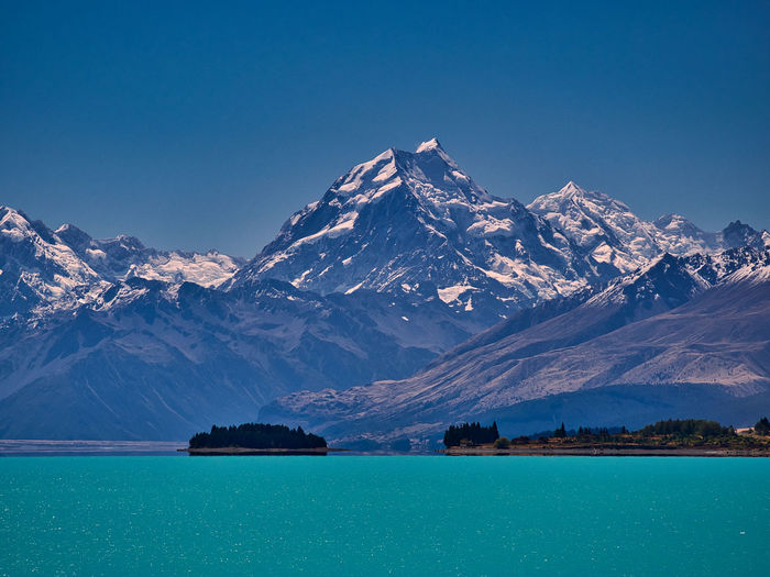 Scenic view of lake by snowcapped mountains against clear blue sky