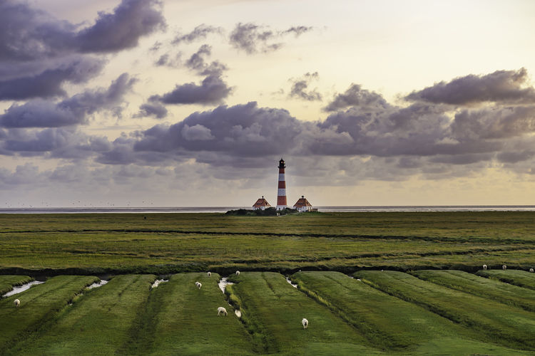 Distant view of lighthouse on grassy beach against cloudy sky