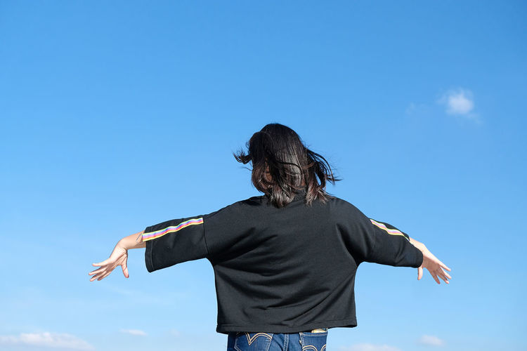 Rear view of woman standing against blue sky