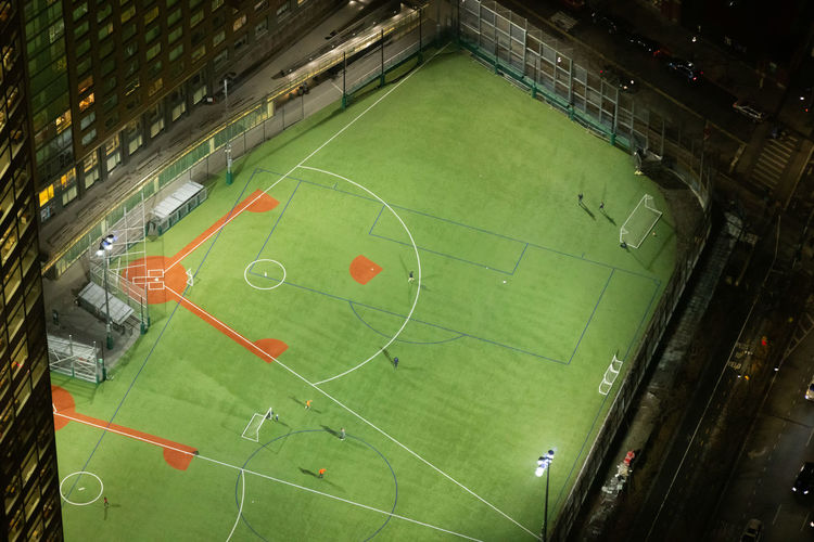 From above of green baseball field with white lines located near modern building on night time in new york city