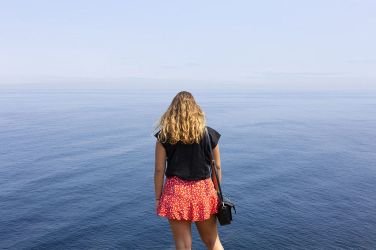 Back view of woman standing in front of the sea against sky