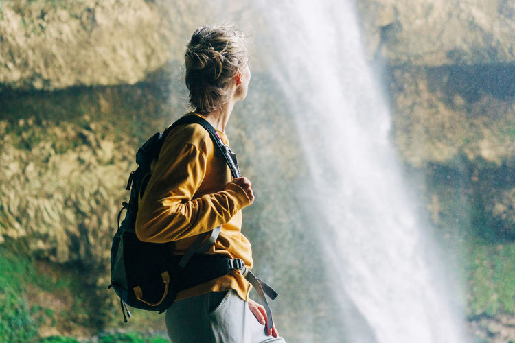 Woman hiker with a backpack in a mountain canyon near a large waterfall.