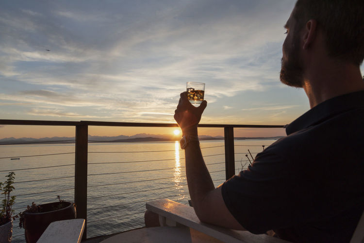 Man with cocktail in hand enjoying sunset from seaside deck.