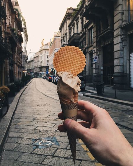 Close-up of cropped hand holding ice cream cone on street in city