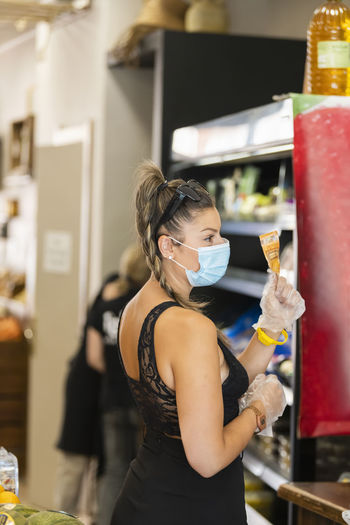 Side view of woman wearing face mask while shopping in supermarket