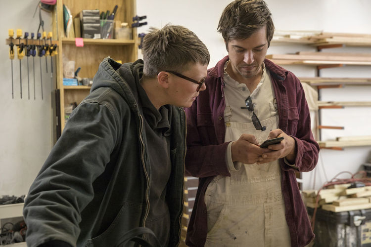 Coworkers discussing over mobile phone while standing in workshop