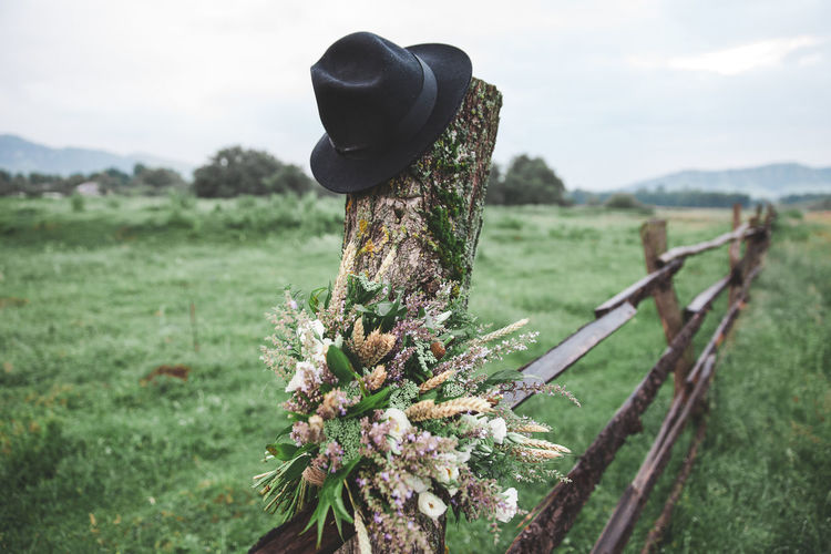 Close-up of flowers and hat on wooden post against sky