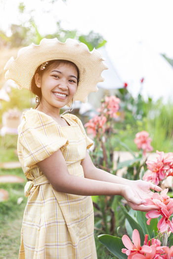 Portrait of a smiling young woman standing by flowering plants