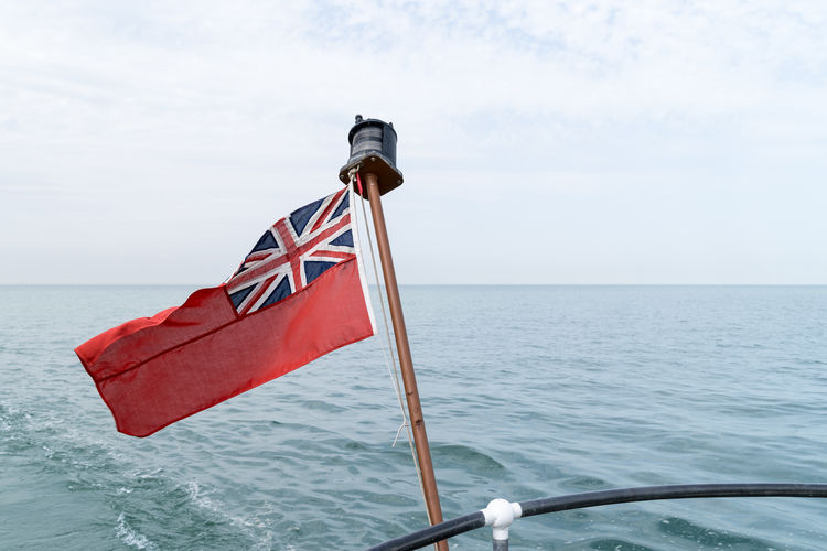An uk red ensign the british maritime flag flown from yacht with the sea and sky behind it