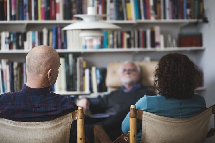 Mature couple discussing with therapist while sitting against bookshelf