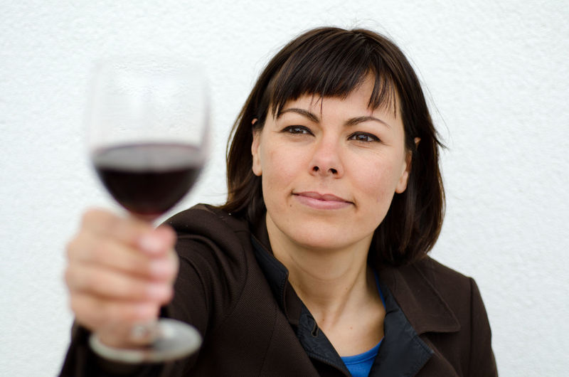 Smiling woman holding wineglass against white wall