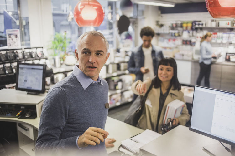 Smiling customer pointing while mature owner looking in electronics store
