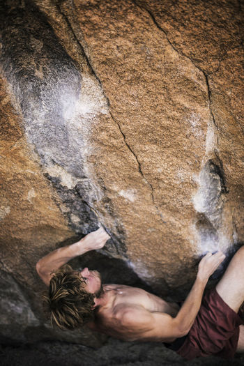 High angle view of shirtless man climbing rock