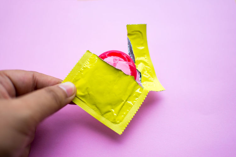 Close-up of man holding condom over pink background