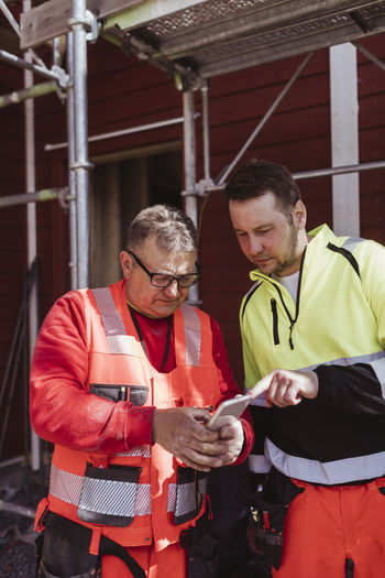 Mature male construction worker discussing over smart phone with colleague at construction site