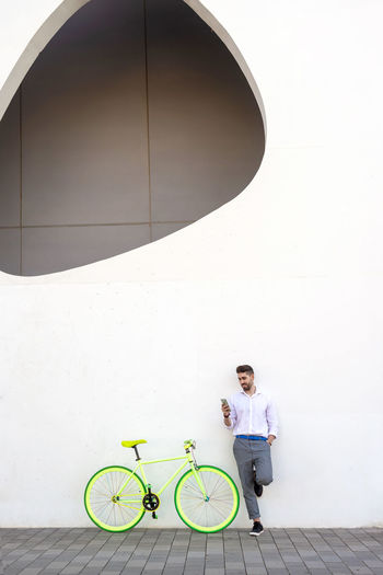 Man with bicycle standing against wall