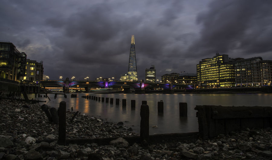 The shard skyscraper in illuminated city by thames river at dusk