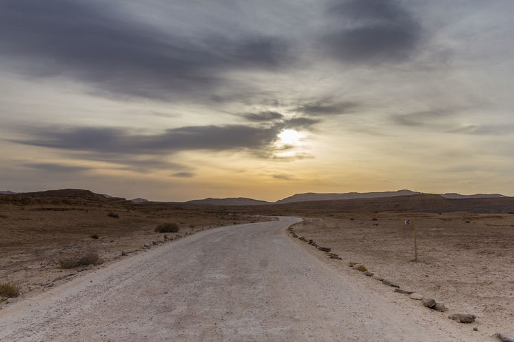 Road by desert against sky during sunset