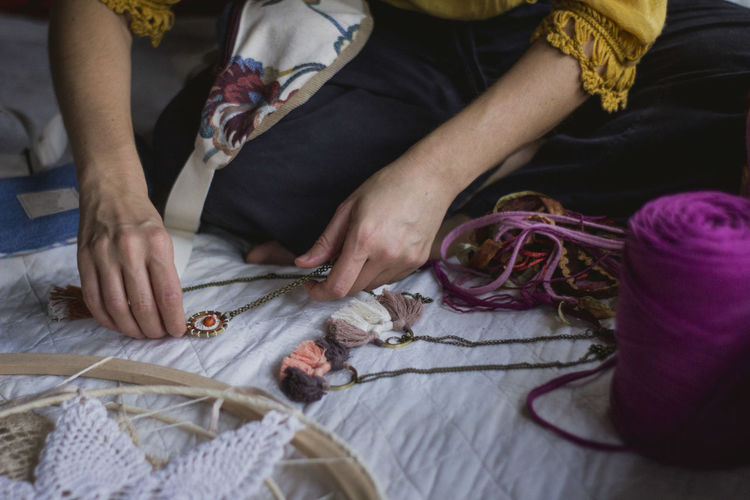 From above of crop female creating handmade dreamcatcher with long threads and accessories sitting in house